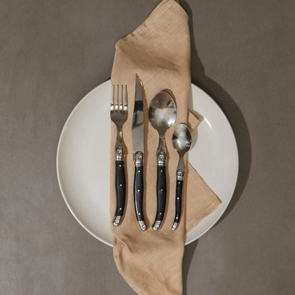 Set of cutlery on a white plate with a beige napkin against a gray background