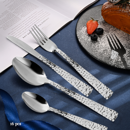 Set of silver cutlery with textured handles on a blue fabric background with a dessert.