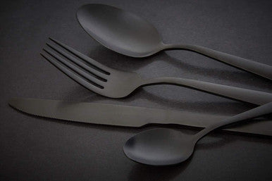 Set of black cutlery including a knife, fork, and two spoons on a dark surface.