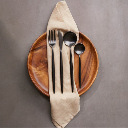 Wooden plate with black cutlery and a beige napkin on a gray background