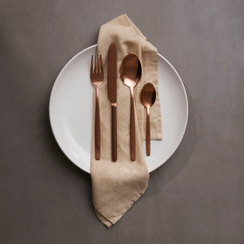 Set of cutlery on a white plate with a beige napkin against a gray background