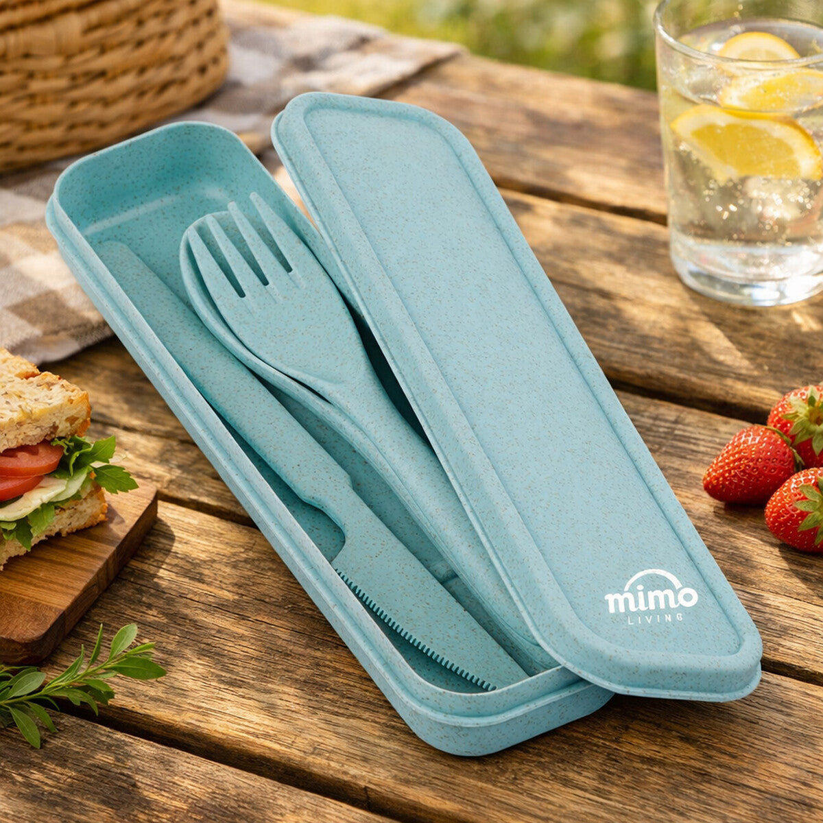 Teal cutlery set with case on a wooden table with a sandwich and strawberries.