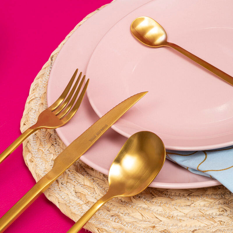 Gold cutlery set on pink plates with a pink background