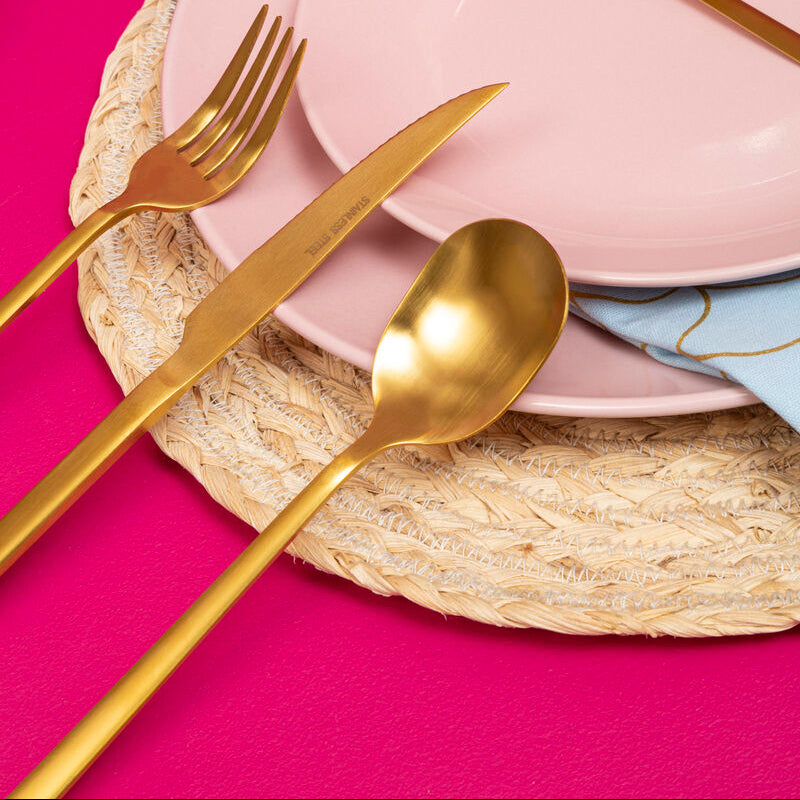 Gold cutlery set on pink plates with a pink background