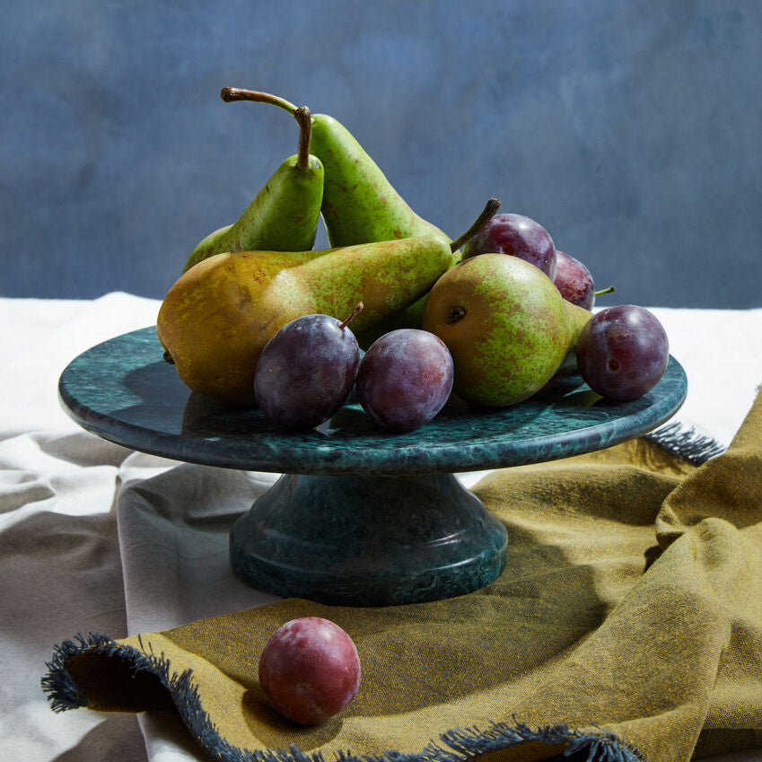 Fruit including pears and plums on a green pedestal against a blue background