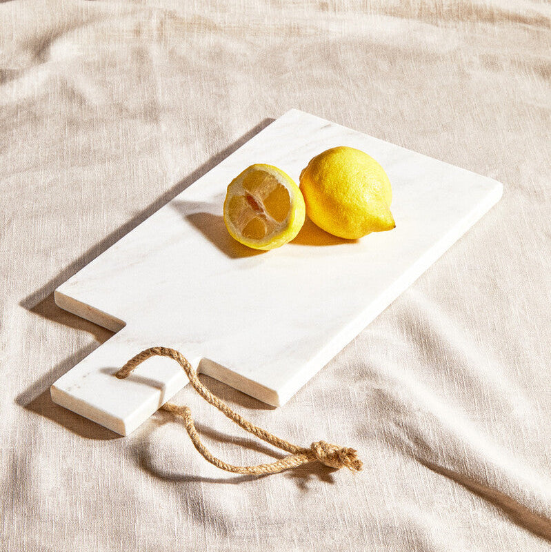 Two lemons on a white stone slab with a rope, placed on a beige fabric background.