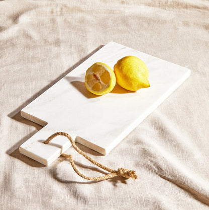 Two lemons on a white stone slab with a rope, placed on a beige fabric background.