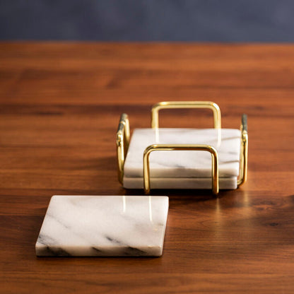 Glass with a drink on a marble coaster, next to a gold holder and marble coasters on a wooden table.