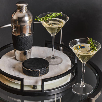 Two cocktail glasses with a shaker on a round marble tray against a dark background