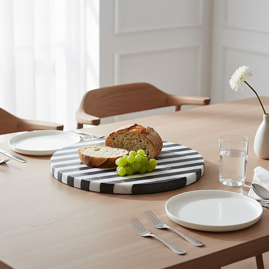 Dining table setting with bread, grapes, and a glass of water on a striped cutting board.