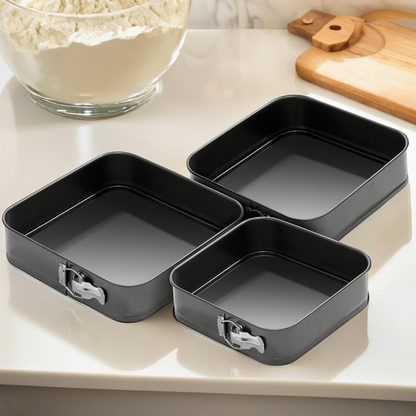 Set of three black rectangular baking pans on a kitchen counter with flour in the background.