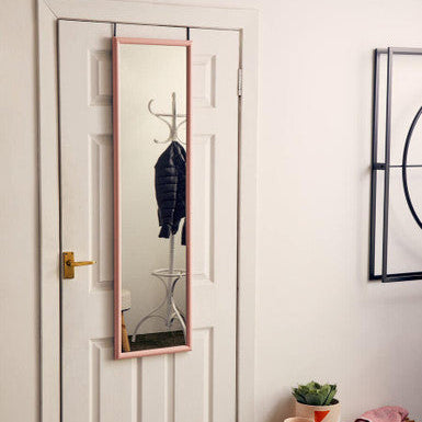 Full-length mirror leaning against a white door in a room with a small table and plant.