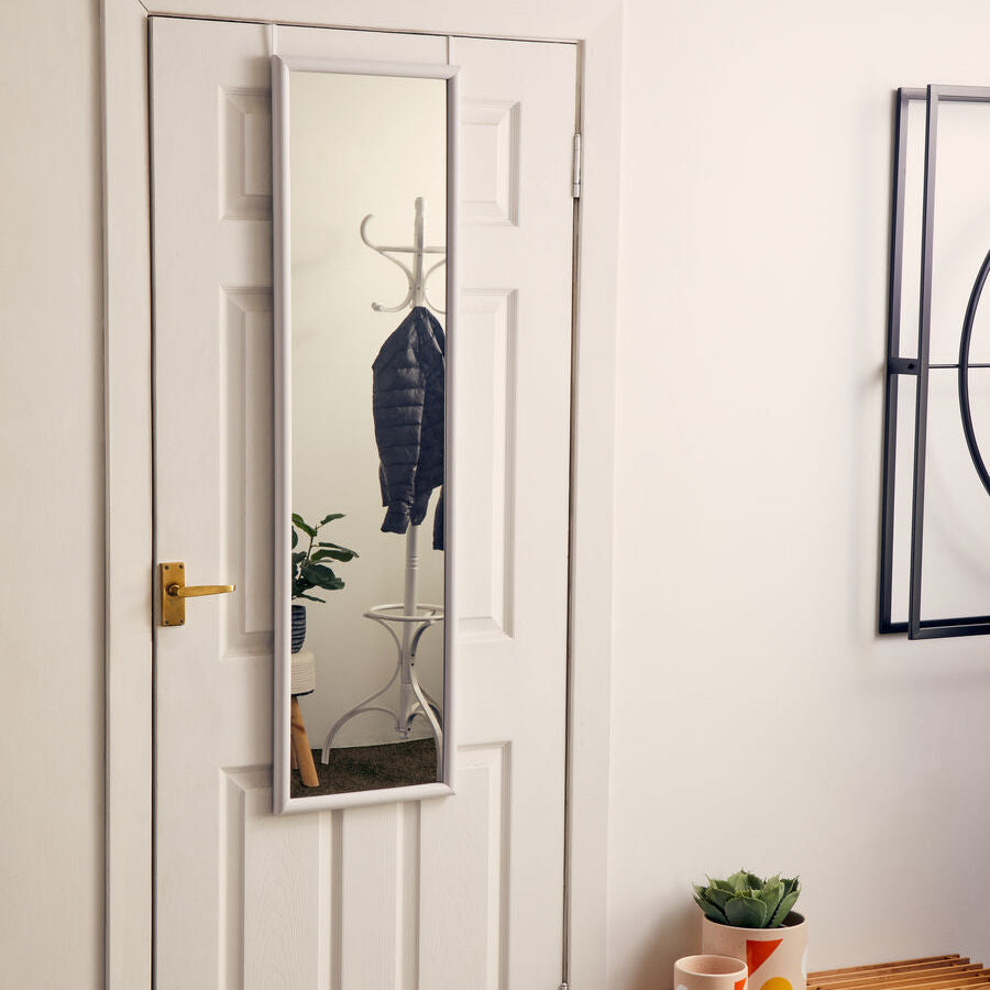 White door with a full-length mirror, plant, and small wooden table in a room.
