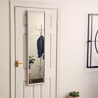 White door with a full-length mirror, coat, and plant in a room.