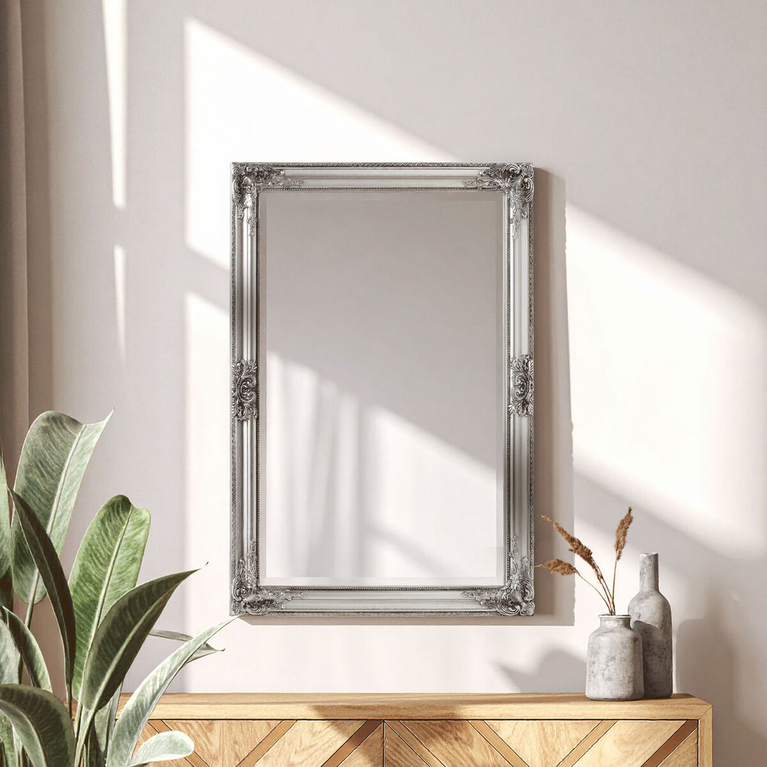 Decorative silver mirror on a wall with a wooden console table and plants.
