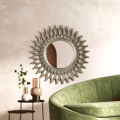 Decorative sunburst mirror on a wall above a green sofa with a side table and plant.