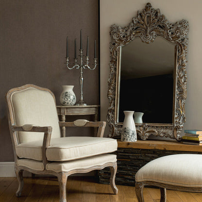 Living room with ornate mirror, chair, and ottoman on wooden floor.