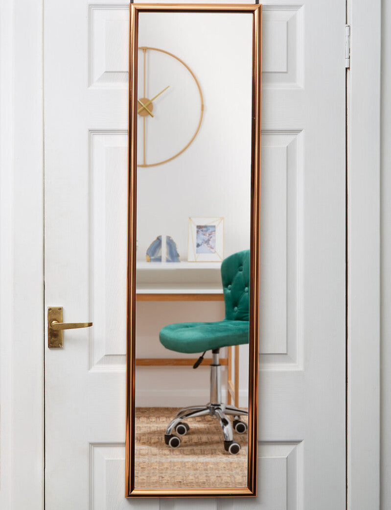 Full-length mirror with gold frame leaning against a white door, reflecting a green chair and decor.