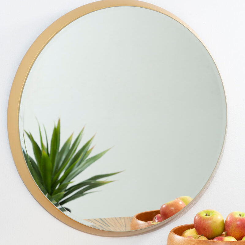 Round mirror with gold frame on a wall above a wooden surface with a bowl of fruit.