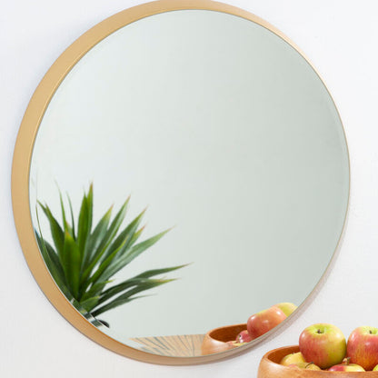 Round mirror with gold frame on a wall above a wooden surface with a bowl of fruit.