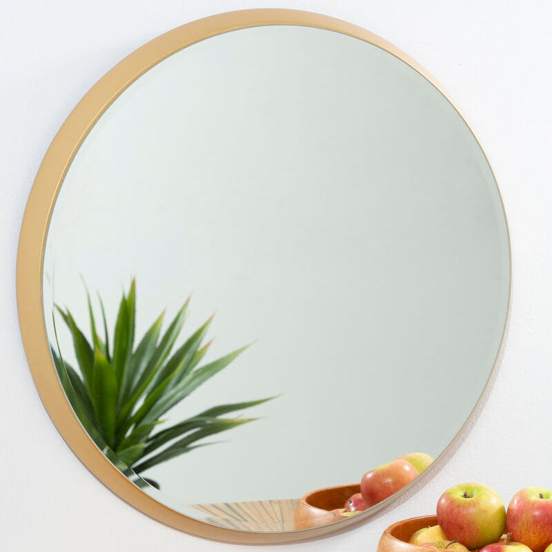 Round mirror with gold frame on a wall above a wooden surface with a bowl of fruit.