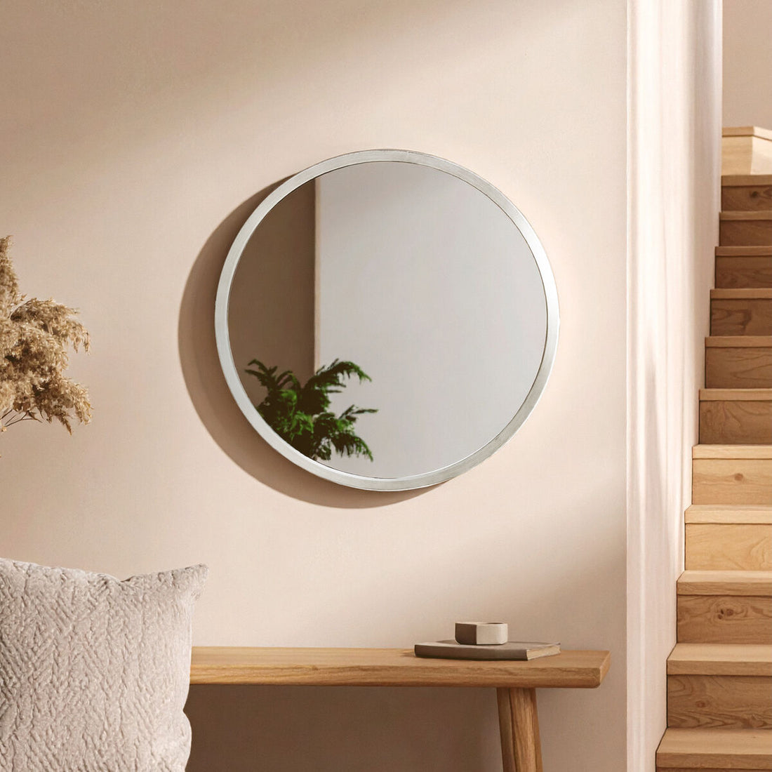 Round mirror on a beige wall above a wooden console table with decorative items.