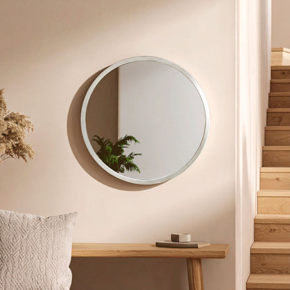 Round mirror on a beige wall above a wooden console table with decorative items.