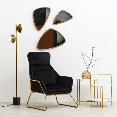Modern black armchair with gold legs in a minimalistic room with wall art and side table.