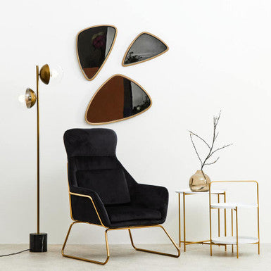 Modern black armchair with gold legs in a minimalistic room with wall art and side table.