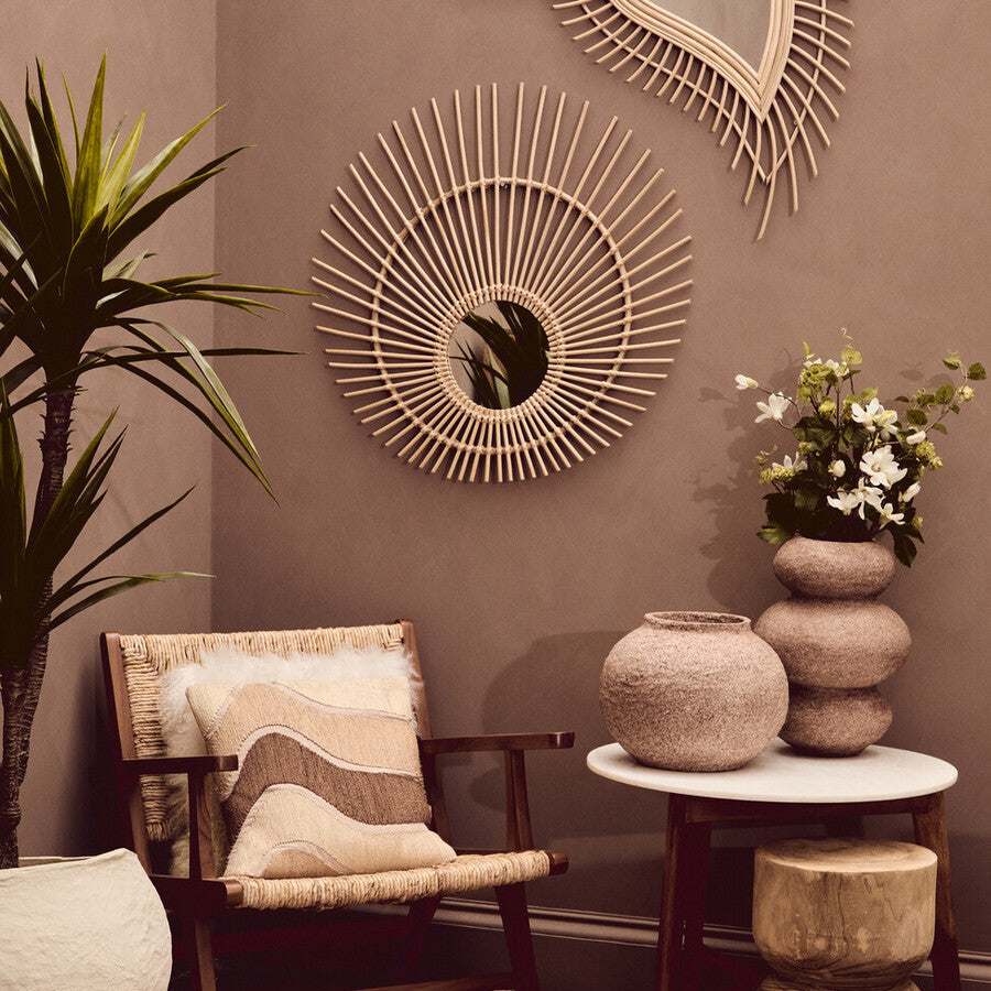 Cozy interior with a wooden chair, round mirror, and decorative items against a brown wall.