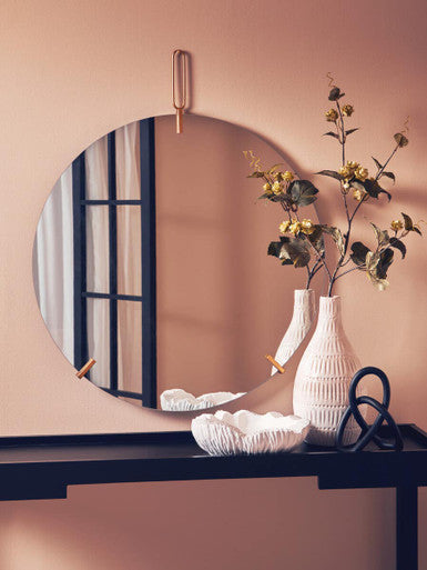 Round mirror on a wall with decorative items including a vase and flowers.