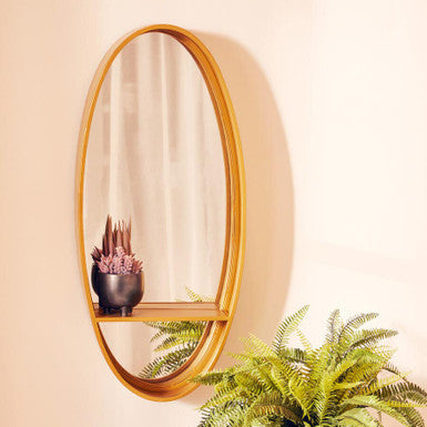 Oval mirror with wooden frame on a beige wall above a potted plant.