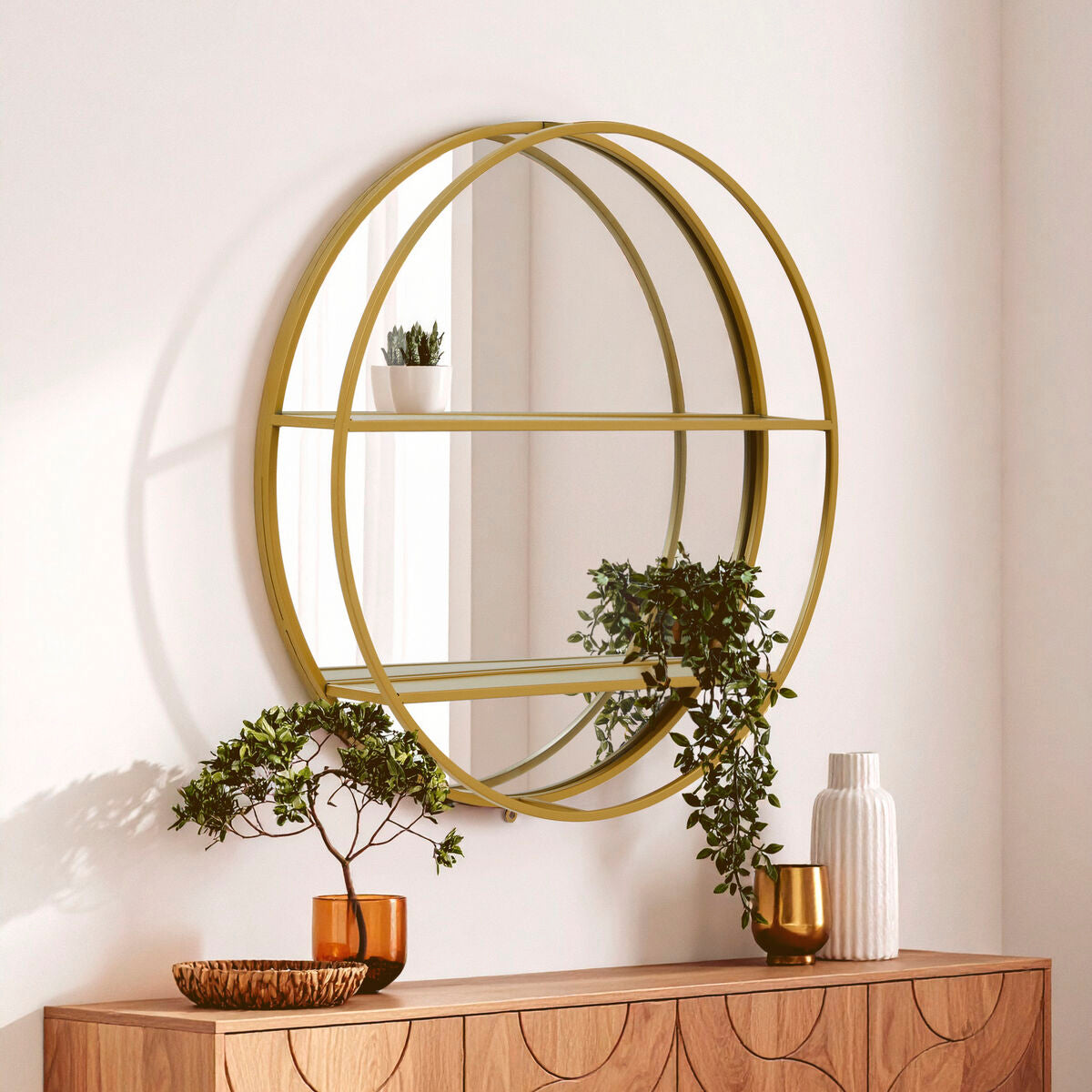 Gold circular mirror on a wall with decorative plants and a wooden console table.