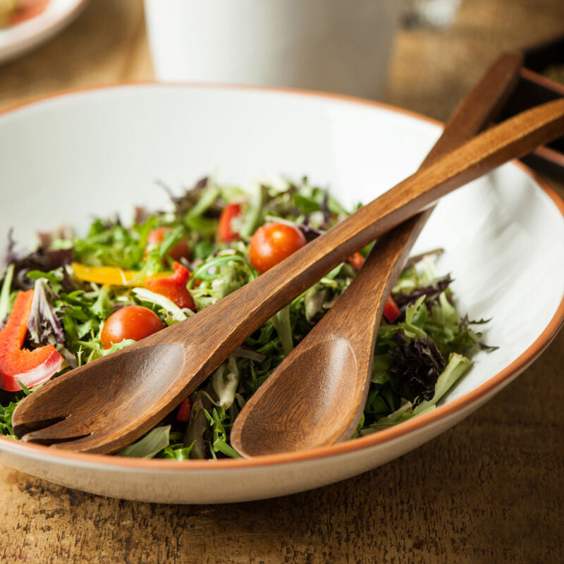Salad in a bowl with wooden spoons on a wooden table