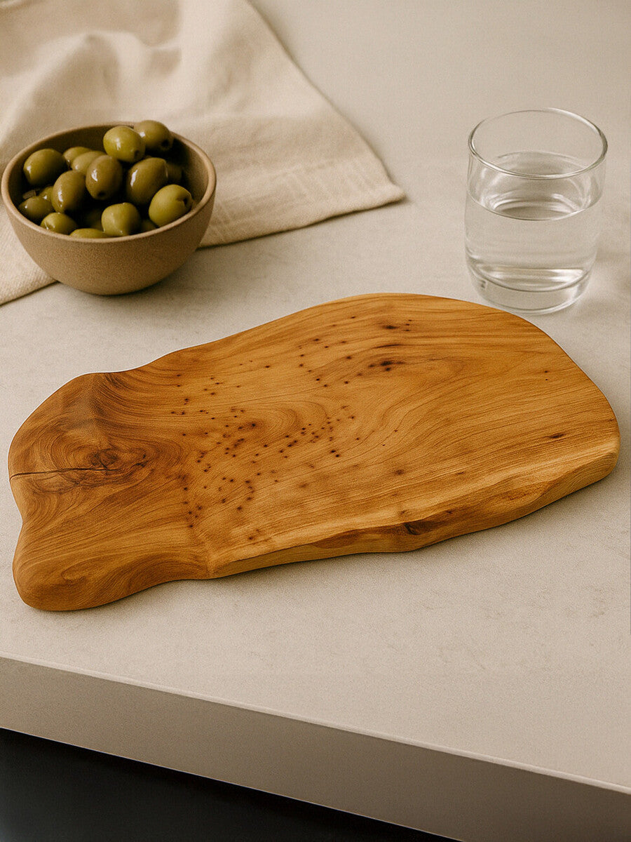 Wooden cutting board on a light surface with a bowl of olives and a glass of water.