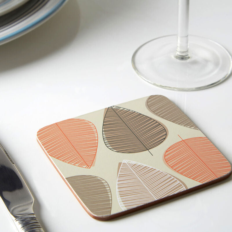 Coaster with leaf pattern on a table with knife, plate, and wine glass.