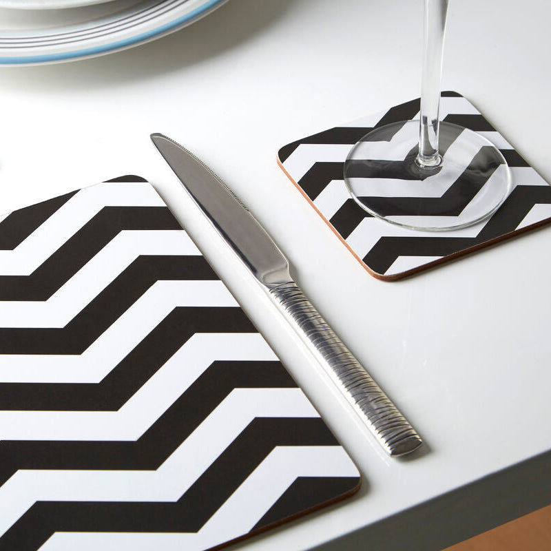 Table setting with black and white zigzag placemat and coasters on a white table.