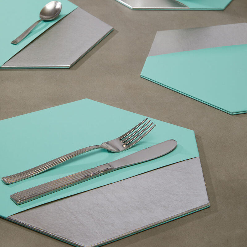 Hexagonal placemats in teal and gray on a table with cutlery and a bowl.