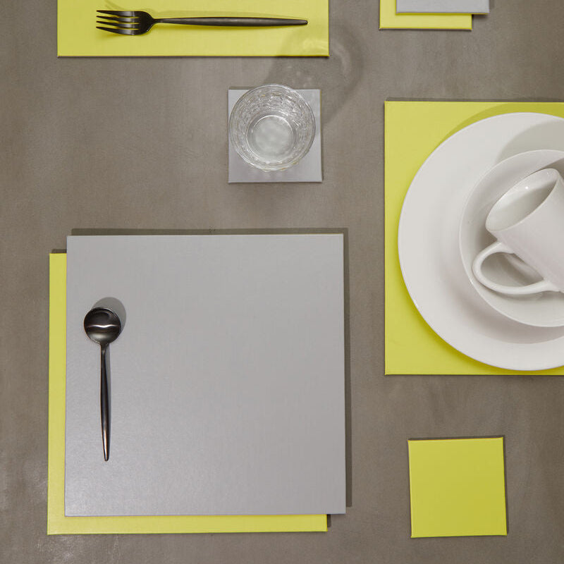 Table setting with yellow and gray napkins, silverware, and a glass on a brown surface.