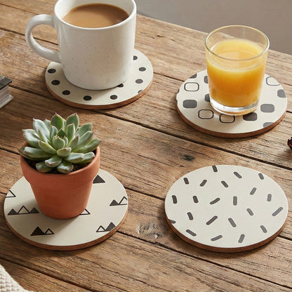 Patterned coasters on a wooden table with a cup, glass, and plant.