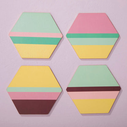Four hexagonal coasters with multicolored layers on a light purple background
