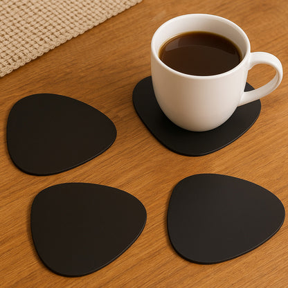 White mug with black liquid on a wooden table with four black coasters.