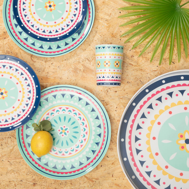 Set of colorful ceramic plates and a mug on a wooden surface with a leaf decoration.