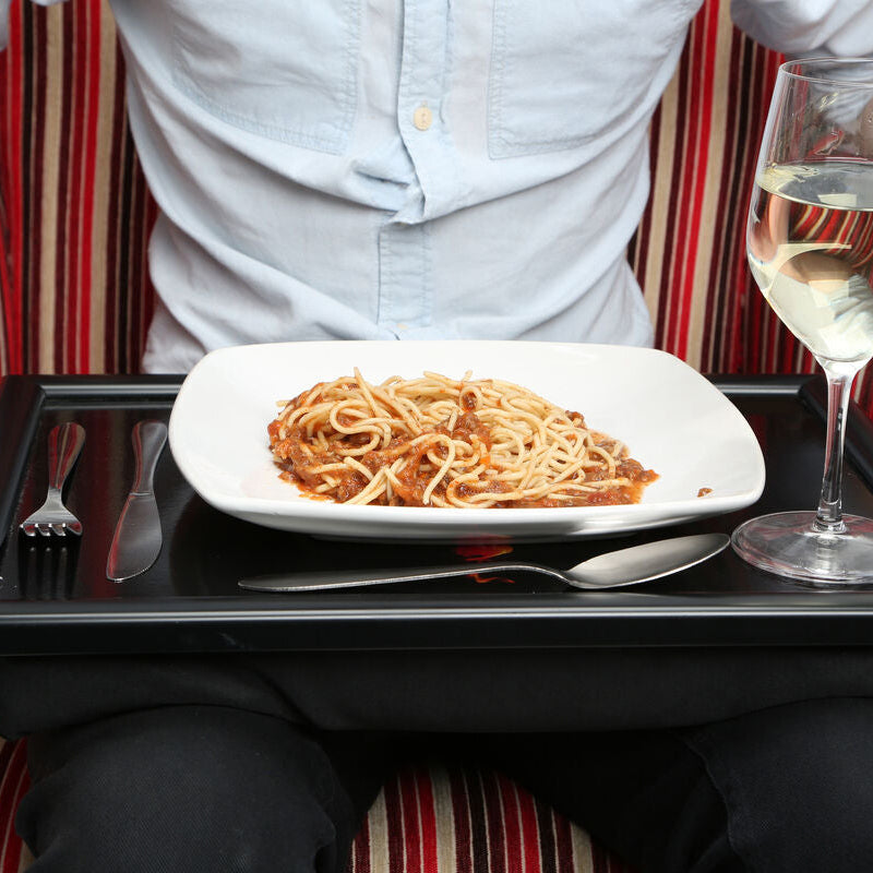 Person sitting on a striped couch with a tray of spaghetti and a glass of wine.