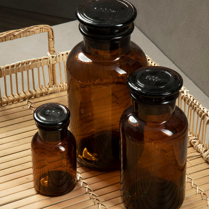 Three brown glass bottles with black lids on a woven surface.