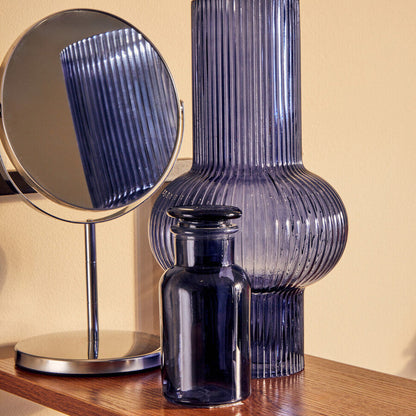 Blue ribbed vase and small black vase on a wooden surface with a mirror reflecting the blue vase.