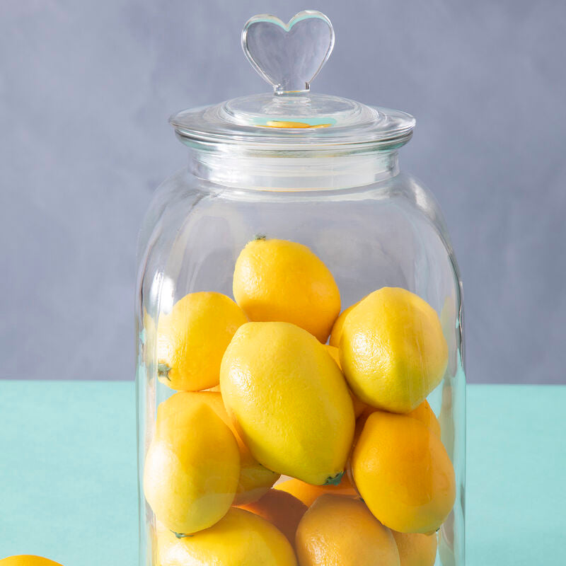 Glass jar filled with lemons on a light green surface with a light purple background