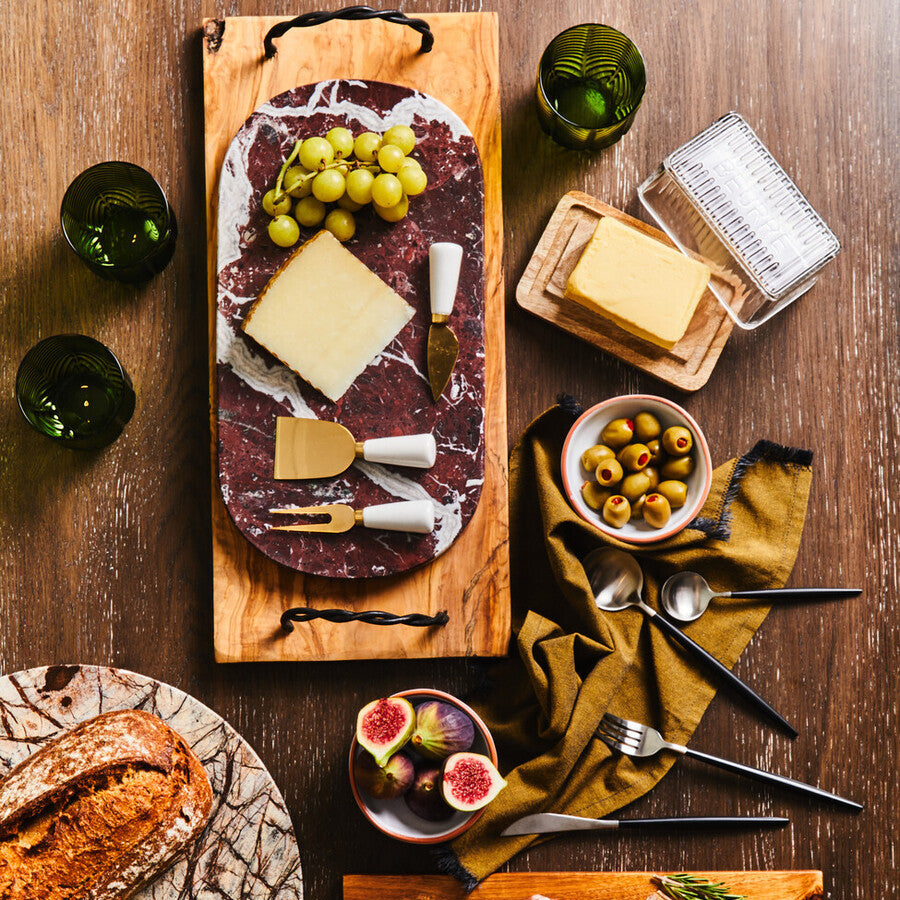 Wooden charcuterie board with meats, cheeses, bread, and fruits on a wooden table.