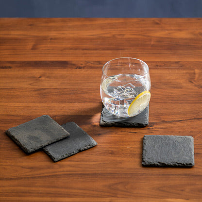 Glass of water with a lemon wedge on a wooden table with black coasters.