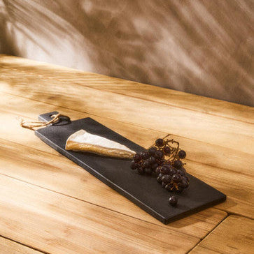 Black slate platter with a piece of cheese and grapes on a wooden surface